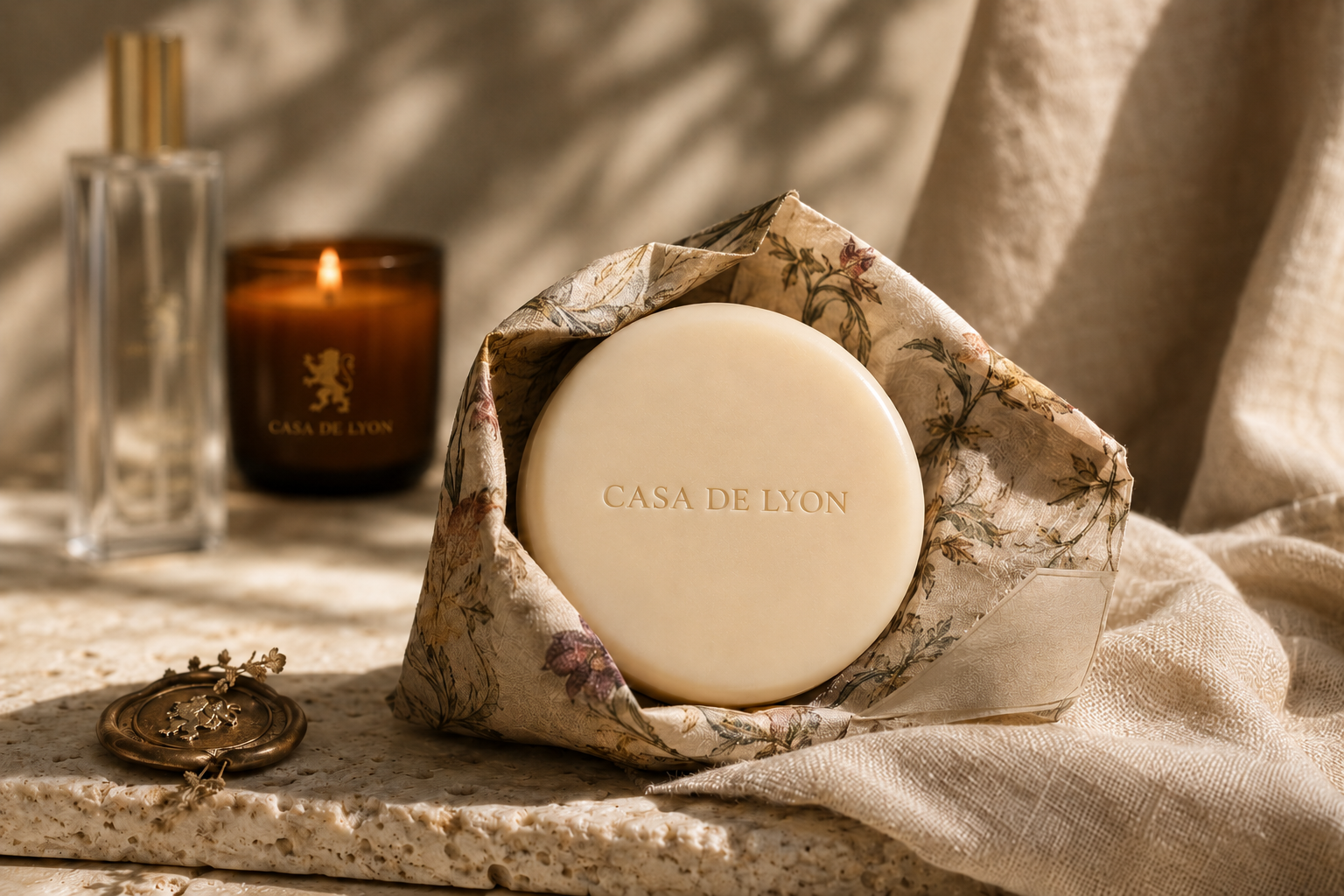 Round ivory Casa de Lyon soap in vintage botanical wrapping with a lit branded candle behind it